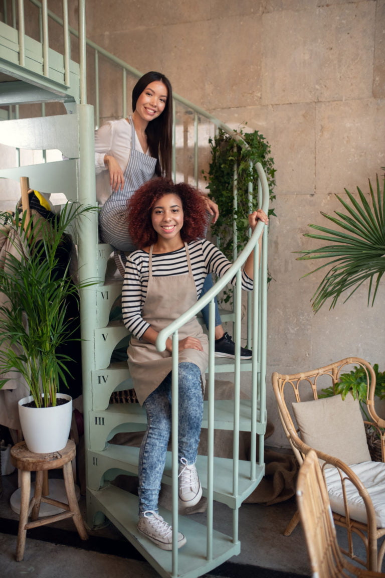 Sitting on stairs. Young but successful entrepreneurs wearing aprons sitting on stairs together